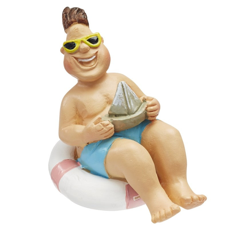Miniatur-Urlauber mit blauer Badehose, gelber Sonnenbrille und Segelboot im weiß-rosa Schwimmreifen