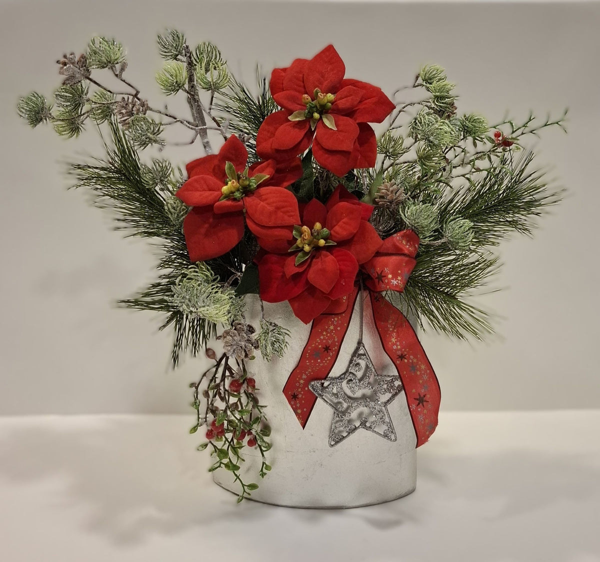 Weihnachtsgesteck in silberner Keramikvase mit roten Blüten, roter Schleife und Dekostern – Gesamtansicht