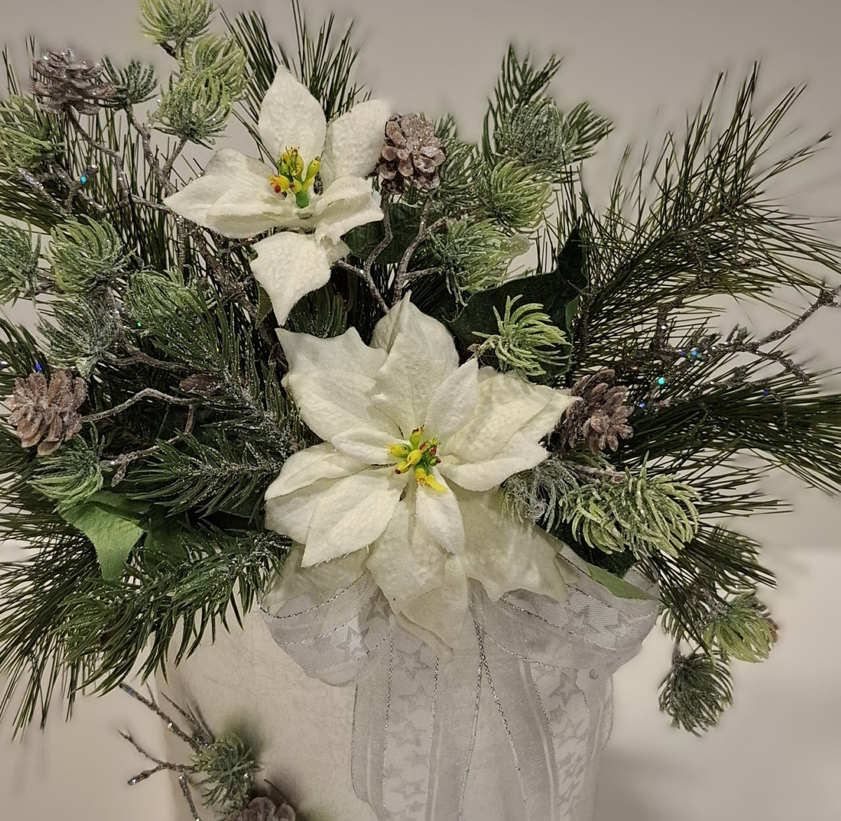 Detailansicht der weißen Blüten, Zapfen und hellen Schleife im Weihnachtsgesteck