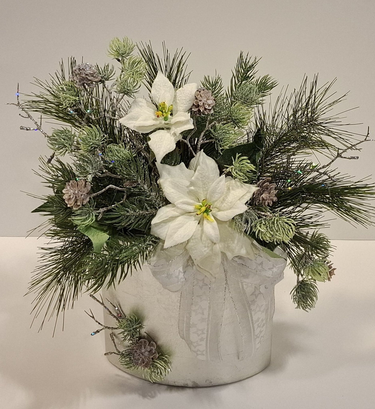Weihnachtsgesteck mit weißen Blüten und grünen Zweigen in silberfarbener ovaler Keramikvase