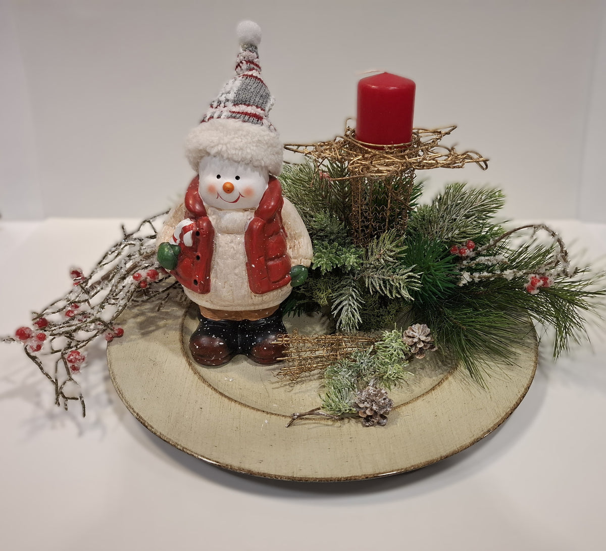 Weihnachtsgesteck auf goldfarbenem Teller mit Schneemann, roten Beeren und roter Kerze